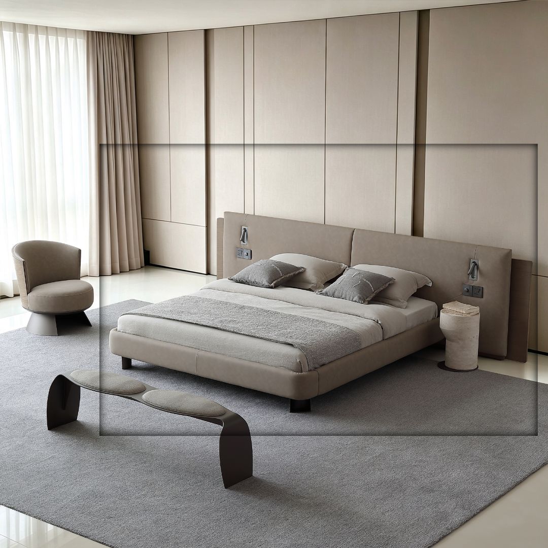 A modern minimalist bedroom featuring a low-profile platform bed with a light beige upholstered frame and matching headboard, styled with gray bedding and pillows. The room has a large gray rug, a matching curved bench, a round armchair, and a textured side table, all set against a beige paneled wall.