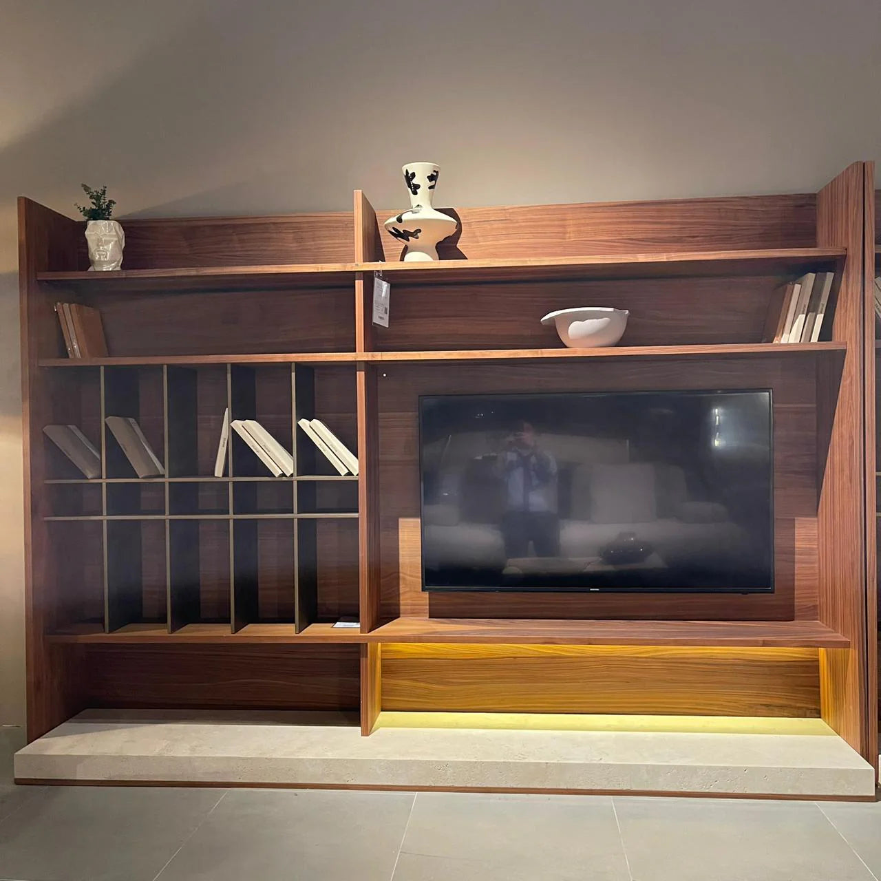 Display of the Edessa wall unit bookshelf and TV block in a modern home, showcasing sleek wood finish and organized storage space.