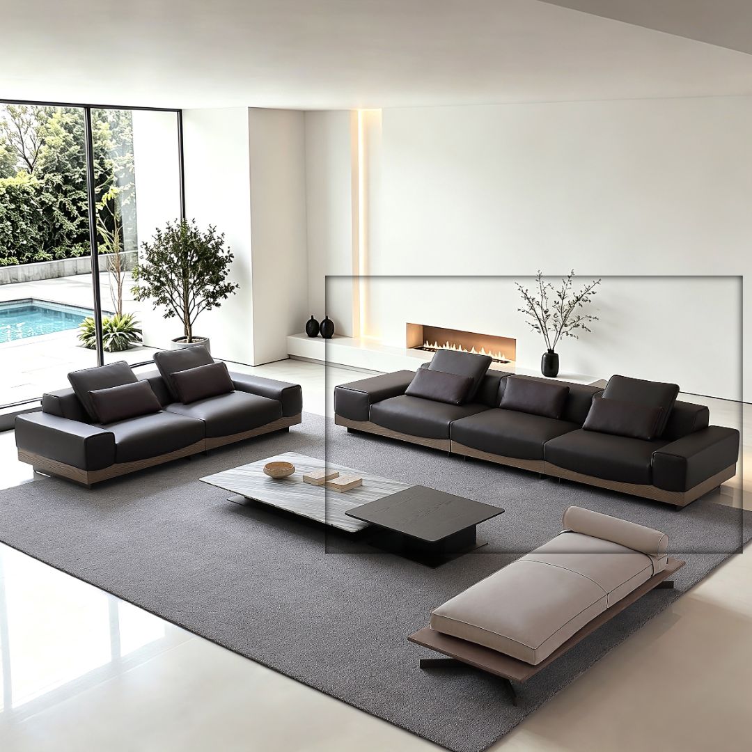 A modern living room scene showing a dark gray sectional sofa, a matching loveseat, and a chaise lounge arranged on a large gray rug. The furniture has dark charcoal upholstery with light wood bases, set in a bright minimalist interior with a pool and windows in the background.