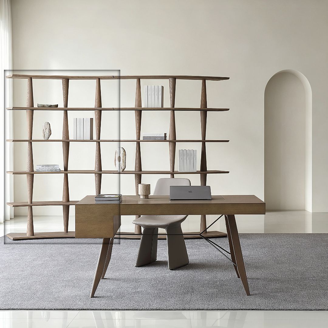 A modern wooden writing desk with angled legs and a matching wooden side cabinet, styled in a minimalist room with a gray chair, a laptop, and a large geometric wooden bookshelf behind it.
