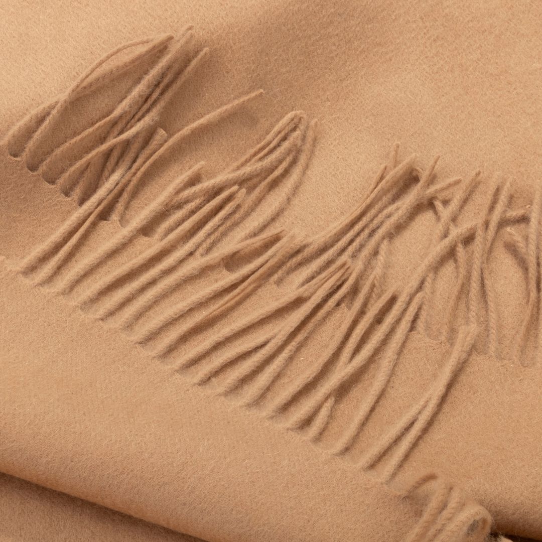 Beige Lana wool scarf by BEACON, stylish and cozy, draped over a surface with soft texture and fringed edges.