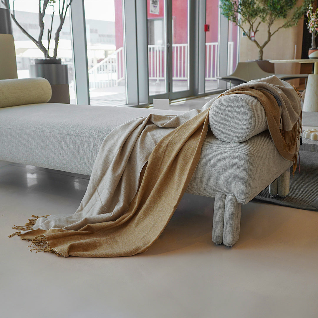 Beige EmberWrap throw blanket by BEACON, 380GSM soft, cozy blanket draped over a sofa for warm comfort.
